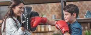 Son with boxing gloves punching pads his mom has on her hands