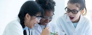Three girls with safety goggles performing science experiment