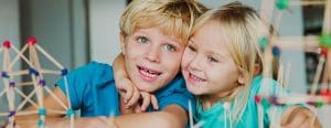 Little girl sitting at a table building with arm snuggly around her brother