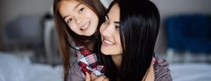 Mom looking at daughter while she holds onto her from the back, both smiling