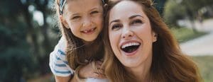Mom with daughter on her back laughing outside