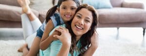 Mom laying on the floor with daughter on her back both smile