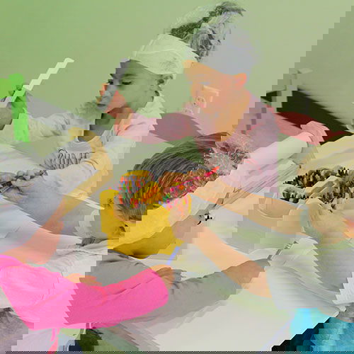 Group of kids sitting at a little table coloring with crayons, they have shower caps on for the lice treatment oil