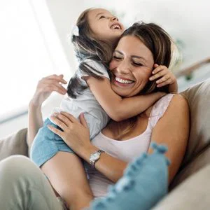 Mom smiling with daughter on her lap with their arms wrapped around each other on the couch